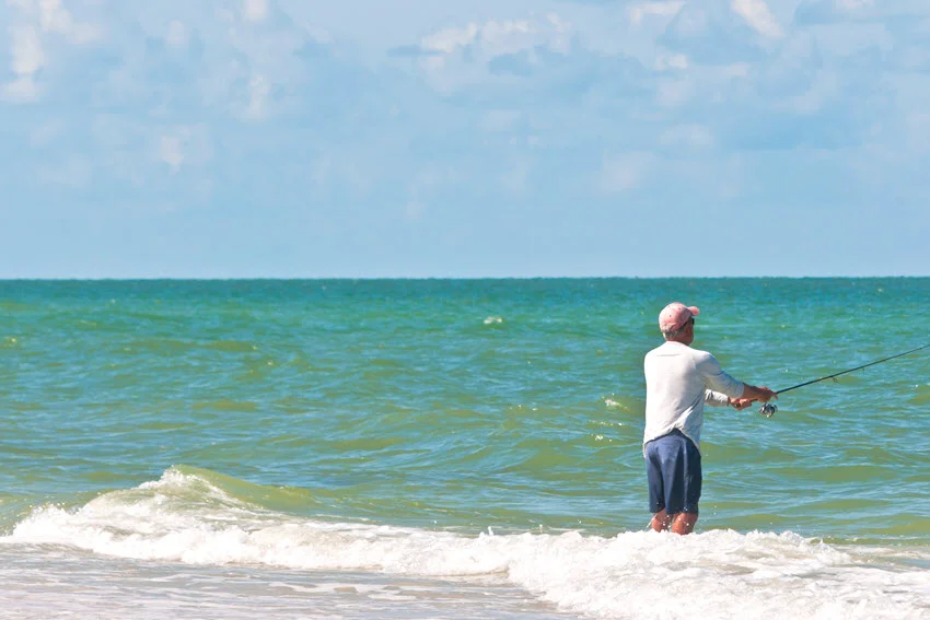 Angler surf fishing in the Gulf of Mexico, standing in breaking waves with a spinning rod pointed toward the open water.