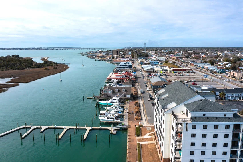 Boats and docks line the waterfront in Morehead City, North Carolina, with waterfront buildings, a broad channel, and a distant bridge.