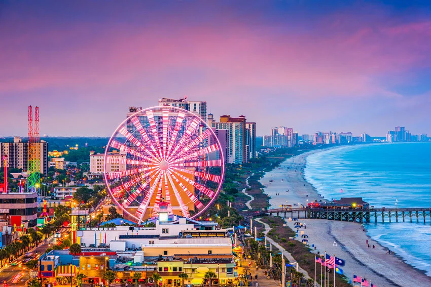 Ferris wheel at Myrtle Beach, South Carolina, with oceanfront hotels, a sandy shoreline, and a pier beside Atlantic waves.