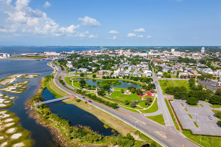 Aerial view of Veterans Memorial Park in Pensacola, Florida, showing curving paths, monuments, a pond, and nearby waterfront neighborhoods.