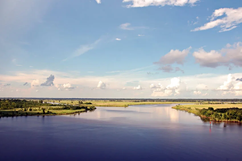 Grassy banks border the Neches River near Beaumont, showing the regional river landscape in the Port Arthur.