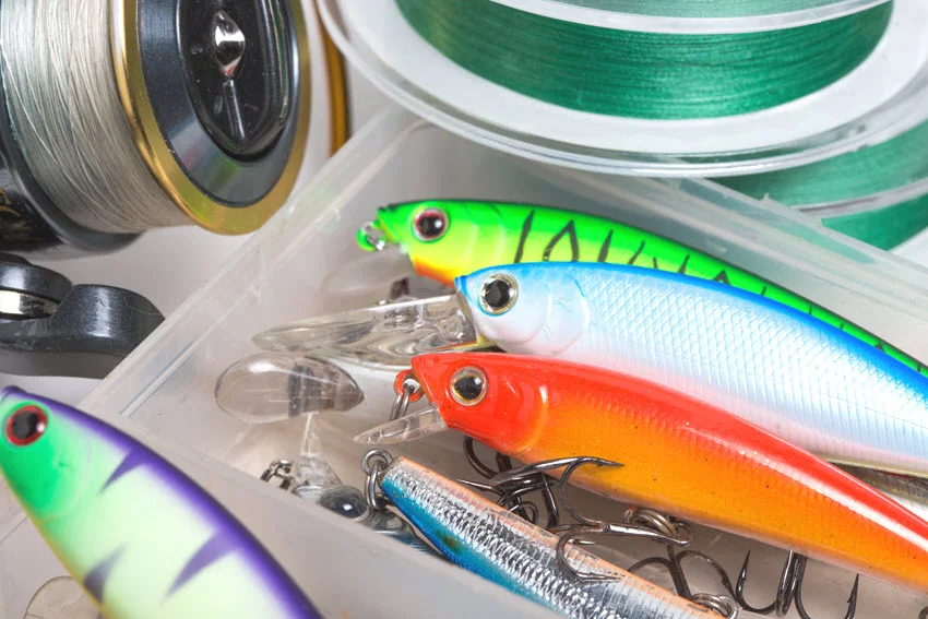 Colorful hard-bodied lures with treble hooks fill a tackle box beside fishing line, artificial lure options for Speckled Trout.