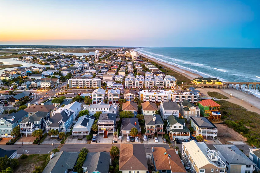 Aerial view of Wrightsville Beach near Wilmington, North Carolina, with coastal homes, a beachfront pier, and Atlantic waves beneath a pastel sky.