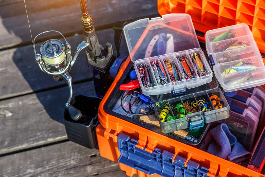 Top-down view of a large angler's tackle box fully stocked with lures and fishing gear, set on a wooden surface.