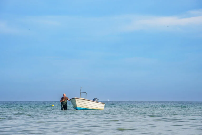 A angler performs flatfishing, by standing in shallow, next to his boat.