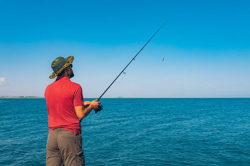 An angler stands on a boat and performs fly fishing in the ocean.