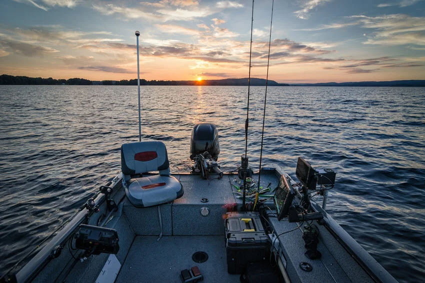 A back view of a private fishing boat filled with equipment, set against the backdrop of calm water and a vibrant sunset.