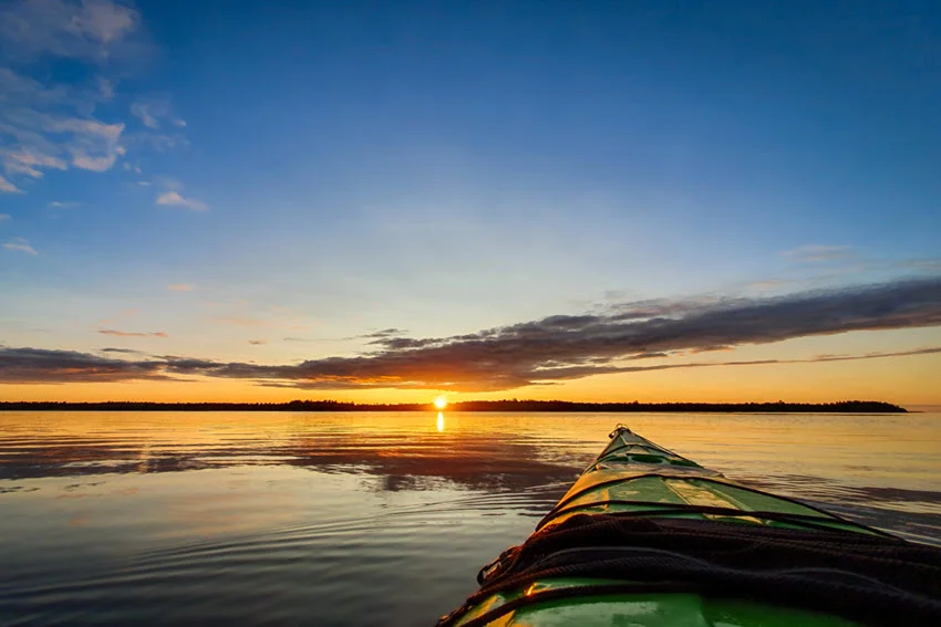 A fishing kayak on a calm lake heading towards the sunset.