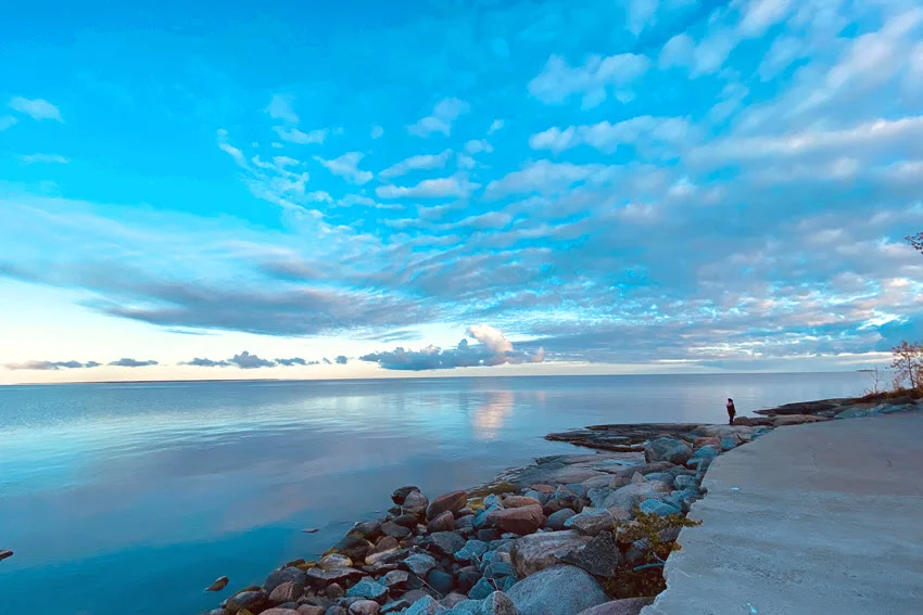 View of Steinhatchee's rocky fishing point in the morning, featuring calm water and an angler in the distance under a soft, serene sky.