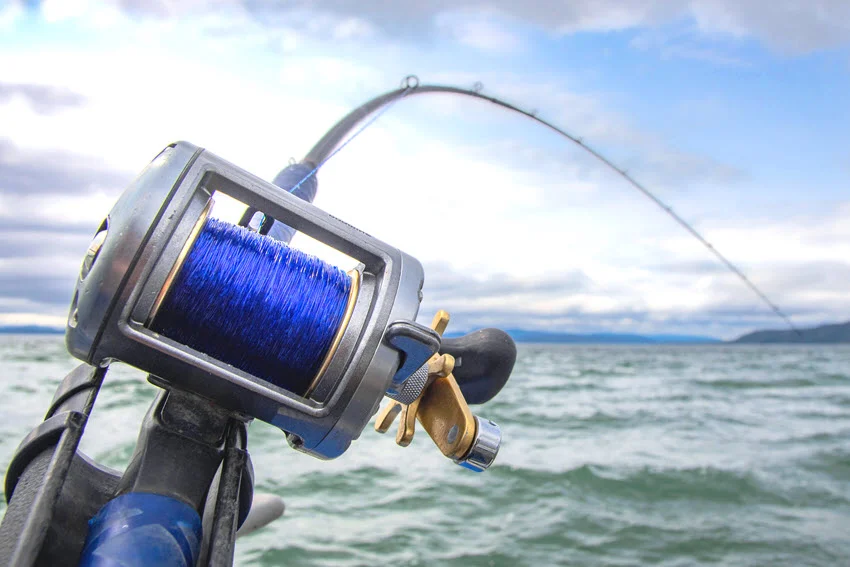 Focused shot of the trolling reel, attached to a boat while moving through the restless sea.