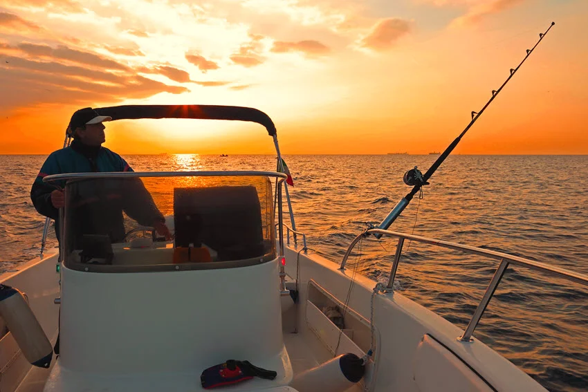 Fishing boat cruising over calm ocean waters at dawn with rods ready for action.