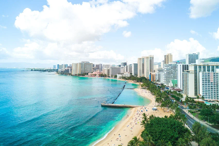 Iconic Waikiki Beach coastline with calm turquoise water and city skyline in the background.