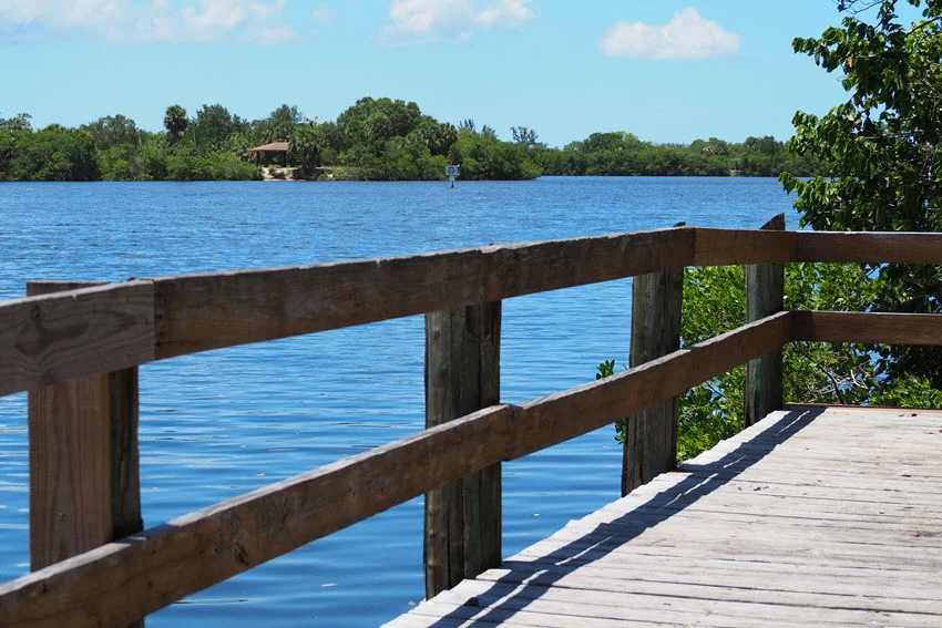 Wooden fishing pier at E.G. Simmons Regional Park with a view of the tranquil blue waters surrounded by lush greenery.