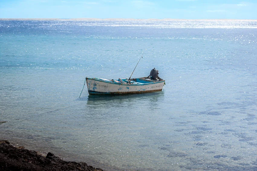 Anchored fishing boat on a calm, empty blue sea, surrounded by peaceful waters and a clear sky, with fishing gear ready on board.