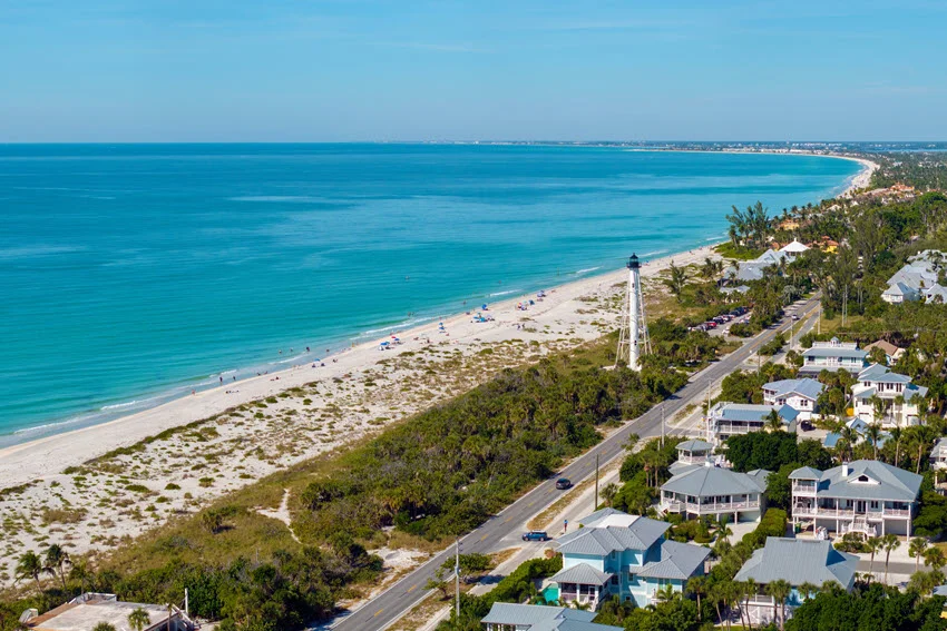 Expensive mansions nestled between green palm trees in the island town of Boca Grande, southwest Florida, with a white lighthouse on the shore guiding commercial vessels.