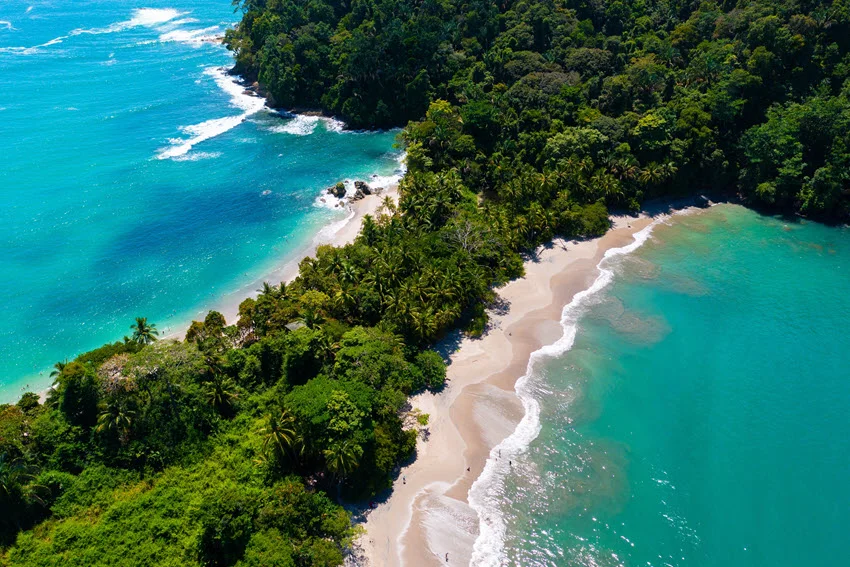 Scenic view of Manuel Antonio Beach in Costa Rica, featuring lush green jungle meeting white sandy shores and turquoise ocean waters, a popular destination for nature and beach lovers.