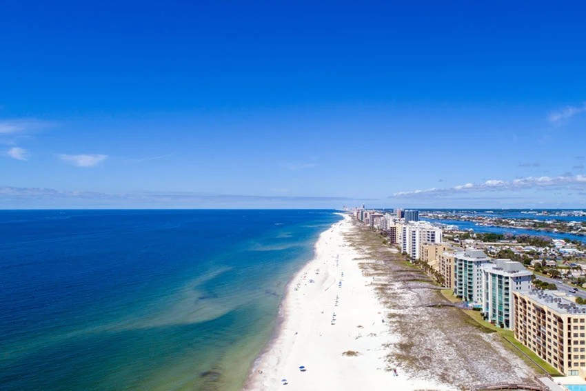 Aerial view of the beach at Perdido Key, Florida, featuring white sandy shores, clear blue waters, and coastal buildings along the Gulf of Mexico.