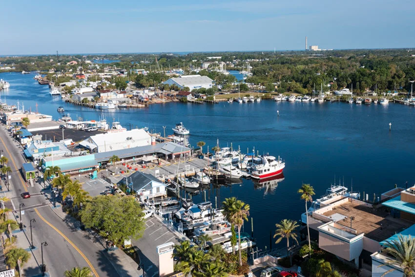 Aerial view of fishing boats docked at a Florida marina with calm inlet water and waterfront buildings.