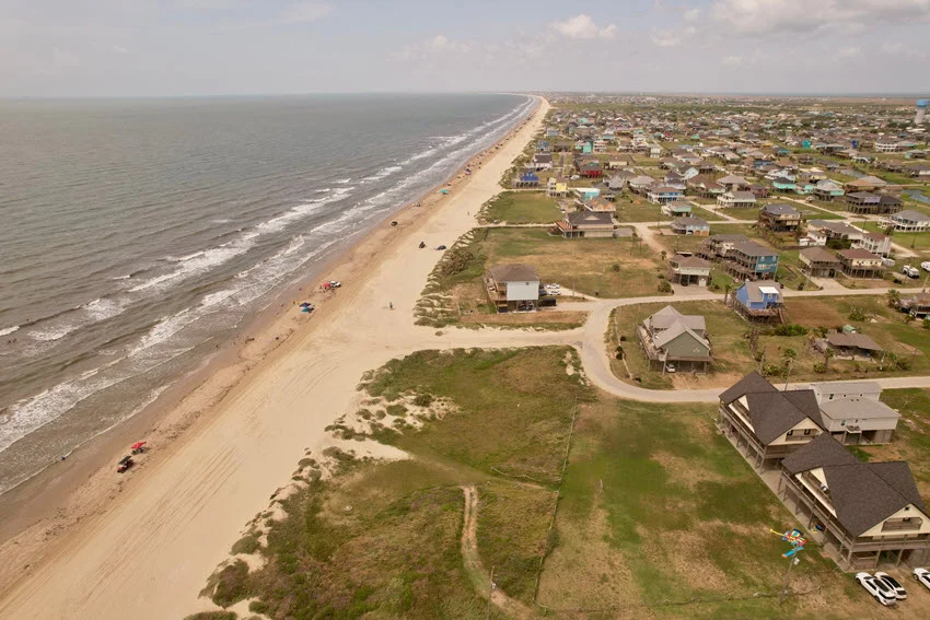 Aerial view of the Bolivar Peninsula coastline, where sandy shores meet the rolling waves of the Gulf under a vast sky.
