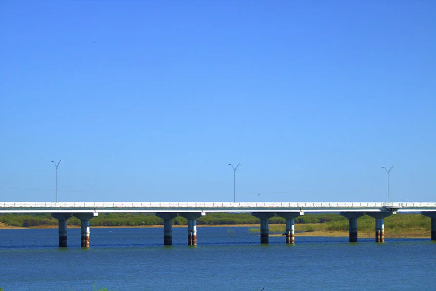 The bridge gracefully arched over Falcon Lake, basking in the warm sunlight of a perfect sunny day. The vibrant blue sky stretched endlessly above, mirroring the serene, deep blue waters below.