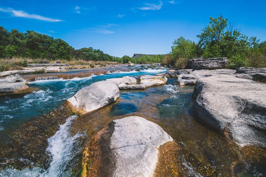 Rock formations and small waterfalls along Devils River, with clear waters flowing over rugged limestone in a serene natural setting.