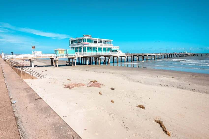 Panoramic view of a fishing pier in Galveston on a sunny day, stretching over the water beneath a clear blue sky.