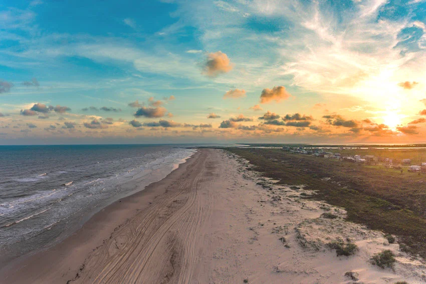 Magnificent aerial view of the sunset casting golden and orange hues over Matagorda Bay Beach, with waves gently touching the shoreline.