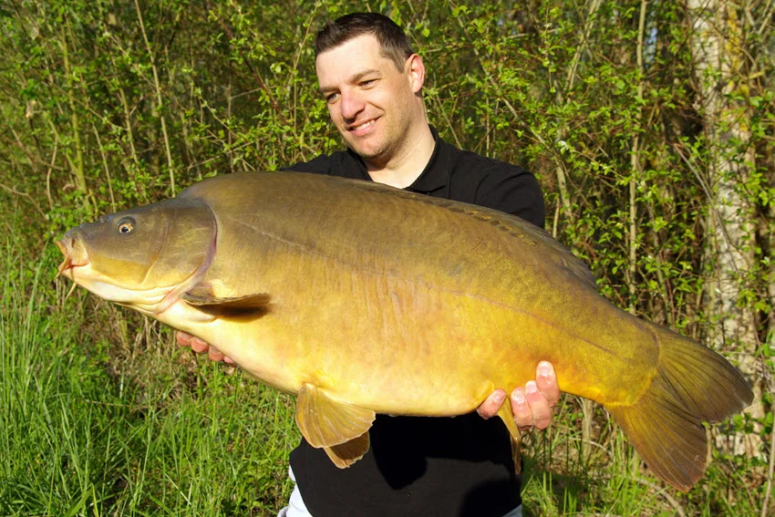 Angler holding a big Leather Carp after a successful freshwater trip, showing the fishs smooth, scale free body and impressive size.