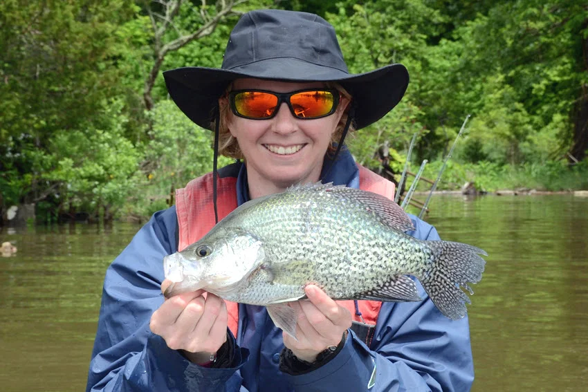 Angler holding a freshly caught Black Crappie near the water, with the fish's speckled sides and broad Panfish body clearly visible.
