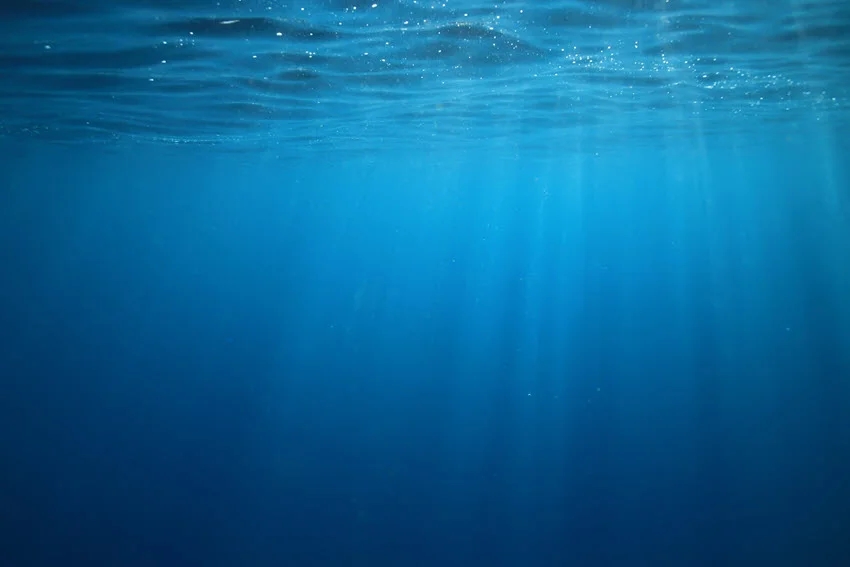 An underwater view of the ocean with the sun's rays spreading through blue water.