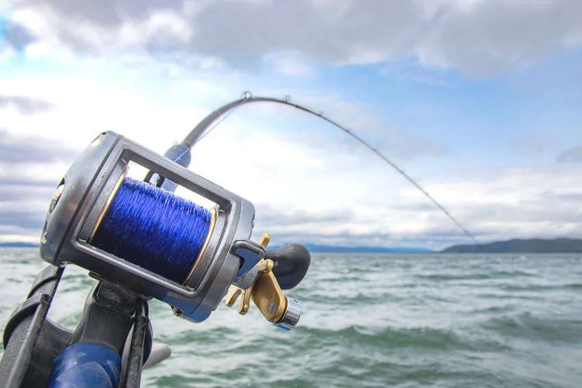 A focused shot of Trolling reels and rods attached to a moving boat with the restless sea and cloudy skies.
