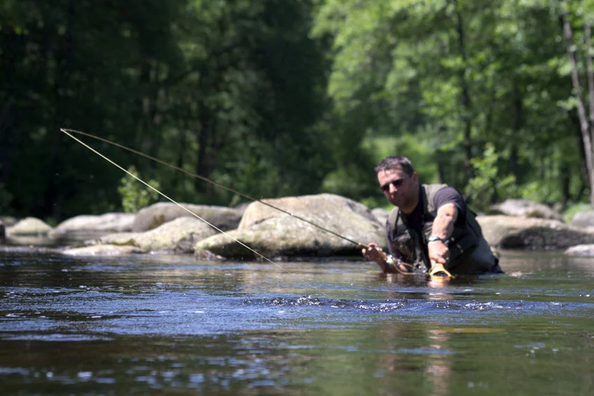 An angler practicing dry fly fishing in a mountain river, surrounded by flowing water and rugged natural scenery.