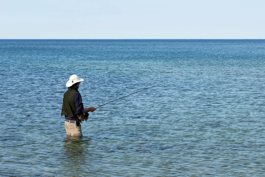 Angler fishing in an open sea coastal area, surrounded by expansive water and distant shoreline.