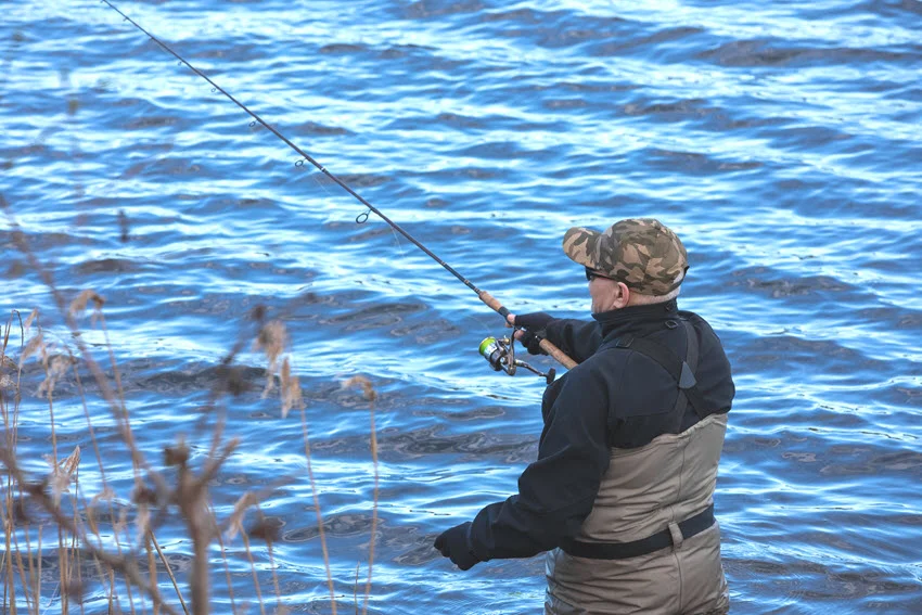 An angler in a wading suit stands in the wavy water of the lake.