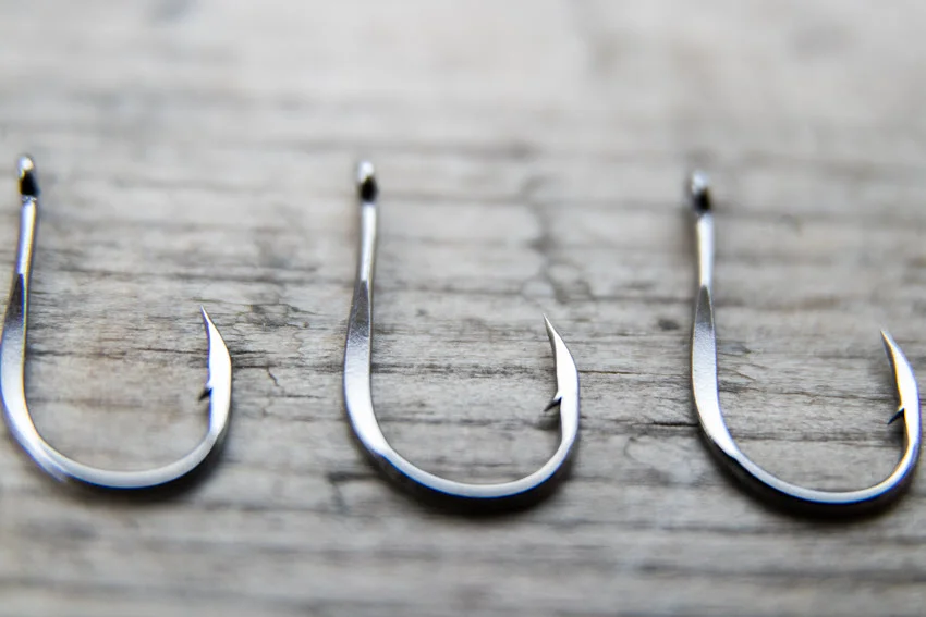 Close-up of fishing hooks arranged on a gray wooden surface, highlighting their sharp points and metallic finish.