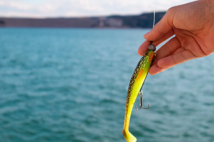 Focused shoot of male angler hands holding spinning bait, with river in the background.