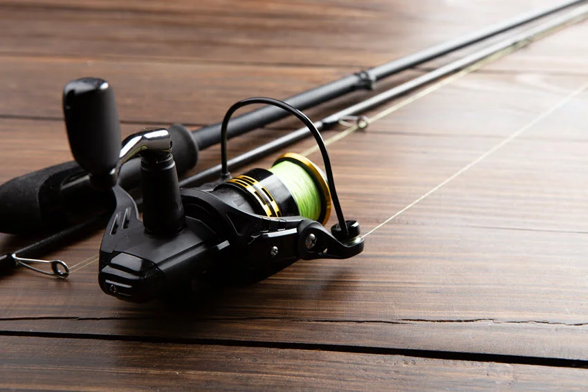 Close-up, focused shot of a spinning fishing rod resting on a wooden surface, highlighting its sleek design and detailed reel.