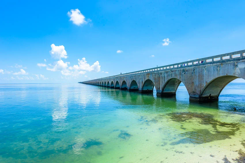 Concrete arches support a historic bridge stretching across clear turquoise water in the Florida Keys, with shallow seabed visible below.