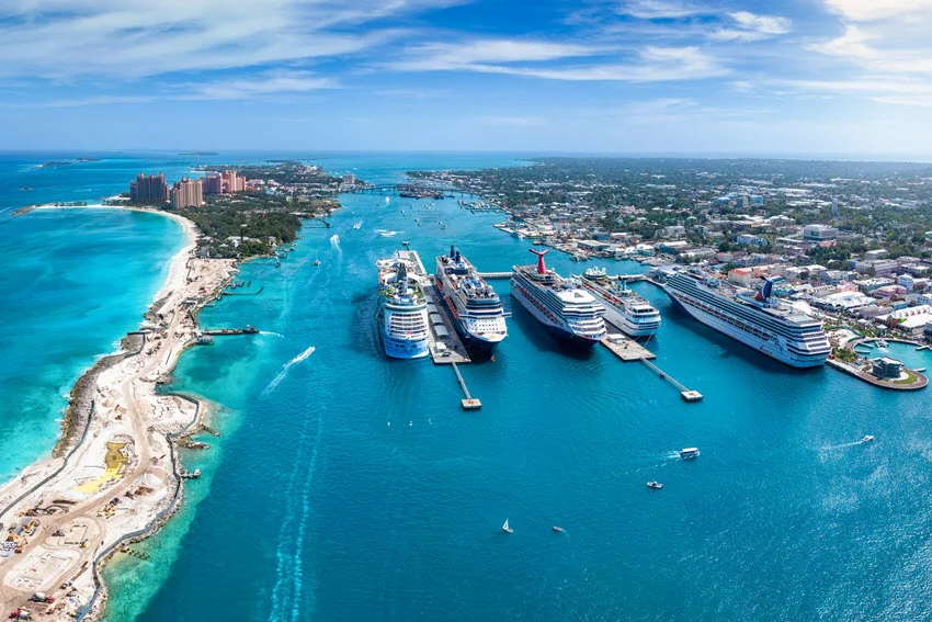 Cruise ships dock at Nassau's port in the Bahamas, with the harbor channel and Paradise Island coastline visible from above.
