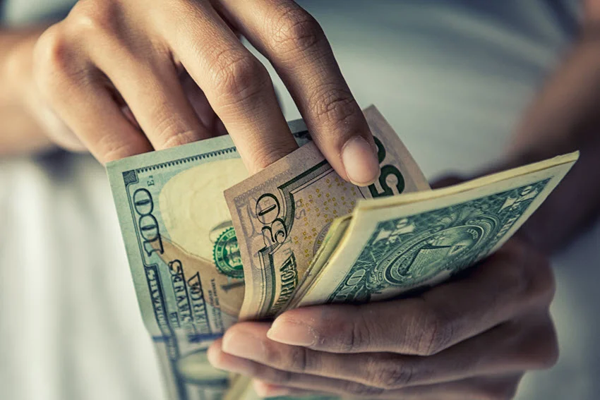 A close-up view of hands counting American dollars, with crisp banknotes visible in detail.