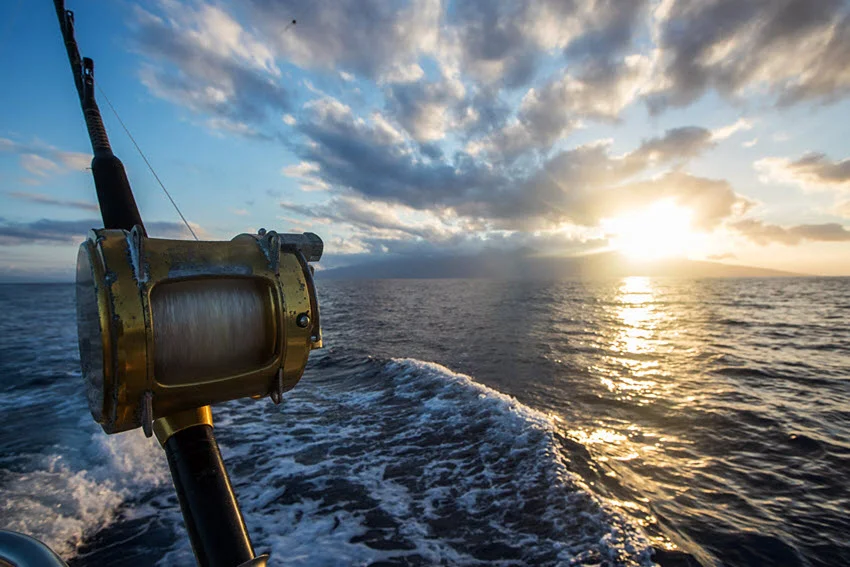 Close shot of a deep-sea fishing reel on a boat with a sunrise in the background, capturing a tranquil moment.