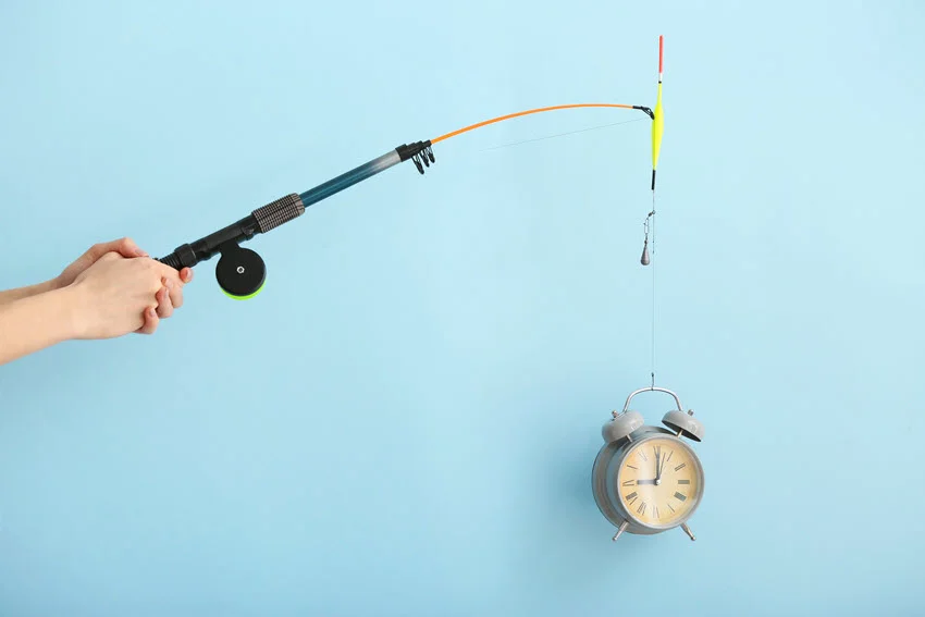 A view of hands gripping a fishing rod next to an alarm clock, set against a colorful background.