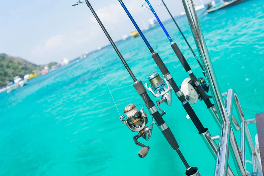 Fishing rods attached to holders on a fishing boat, set up for a fishing trip, with blurry turquoise-blue water in the background.