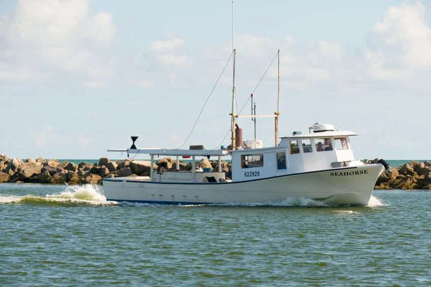 A view of a shrimp fishing boat charter sailing along the Gulf of Mexico coast near St. George Island, Florida, with calm waters and a coastal backdrop.