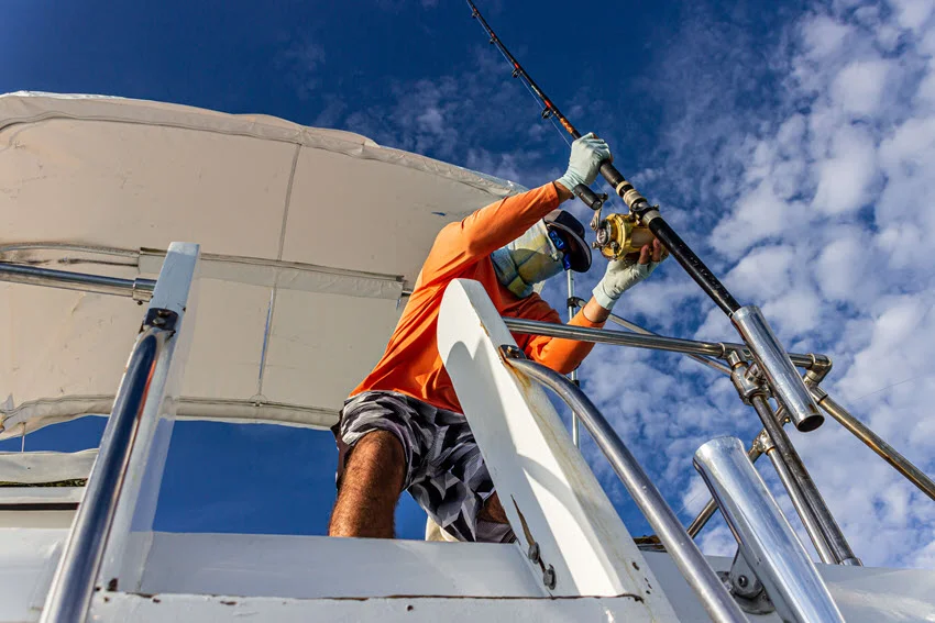 An upward shot of an angler preparing a rod and reel for the next fishing adventure, with a clear blue sky in the background.