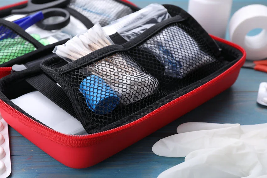 A closeup shot of a red first aid kit on a blue wooden table, with blurred first aid supplies scattered around it.