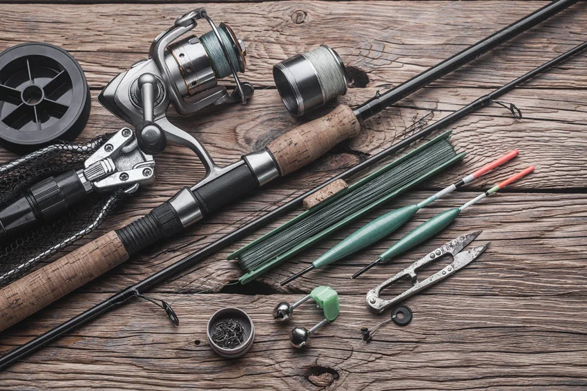 A focused view of fishing tackle arranged for a peaceful fishing trip, including a float, fishing rod, reel, and fishing line on a wooden surface.