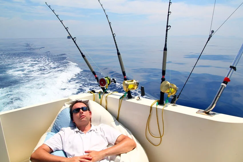 A sailor resting on the boat during summer vacation with fishing rods attached and a backdrop of the blue sea.