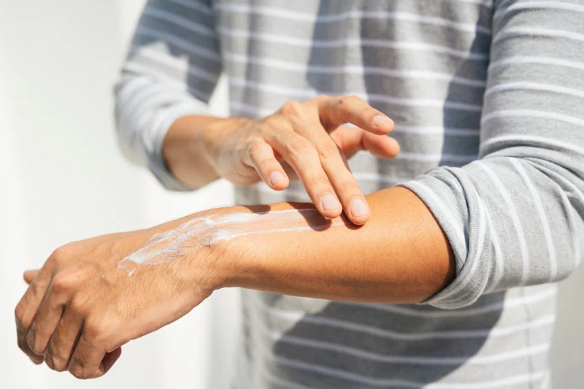 A close shot of a man applying sunscreen lotion to his arms for UV sunlight protection.