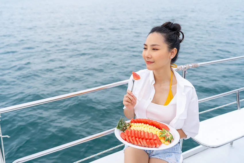 A woman enjoying fresh tropical fruit on a luxury private catamaran yacht during a summer beach holiday.
